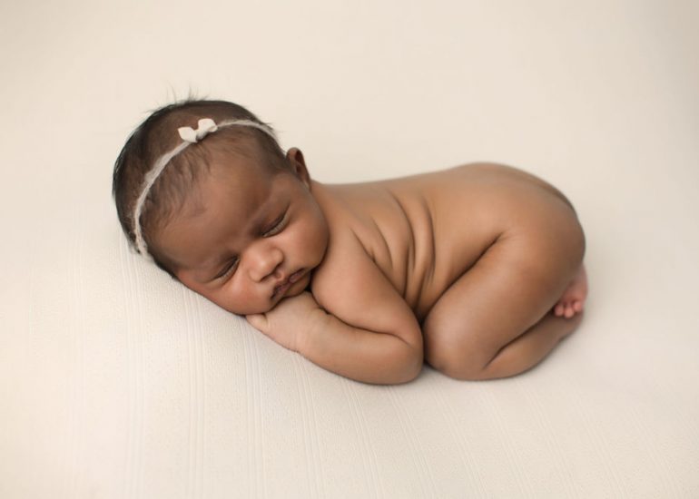 A newborn baby sleeps naked on a white bed in froggy pose after using cloth diaper service Oshawa