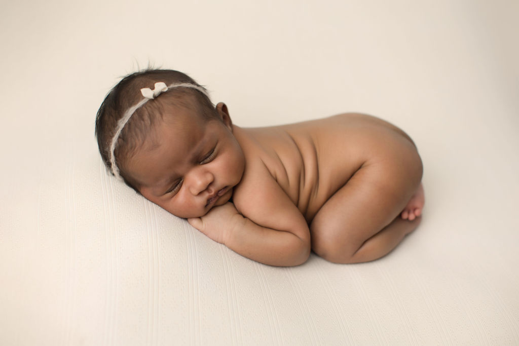 A newborn baby sleeps naked on a white bed in froggy pose after using cloth diaper service Oshawa