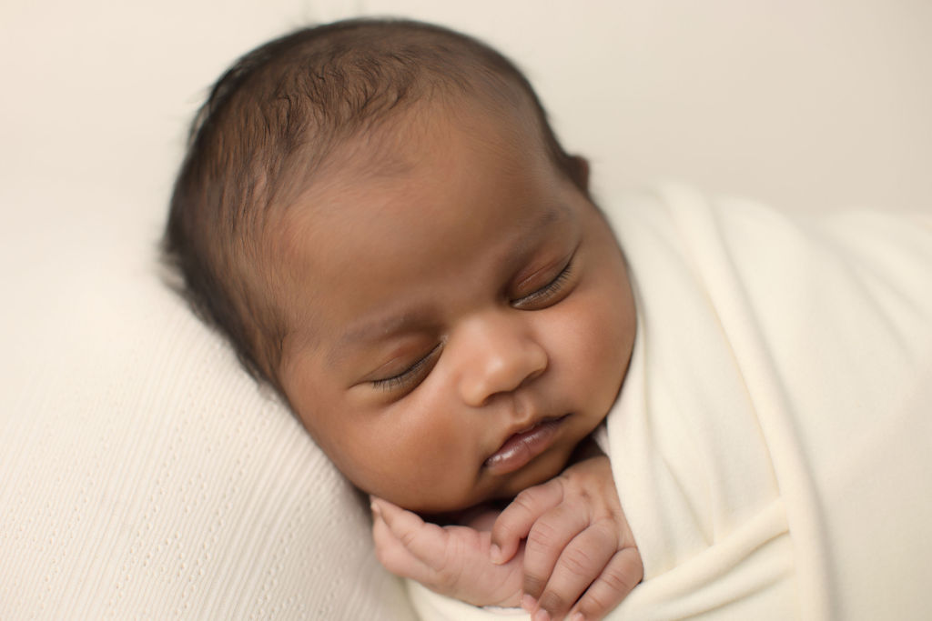 A newborn baby sleeps on its side with hands poking out of a white swaddle after using a doula oshawa