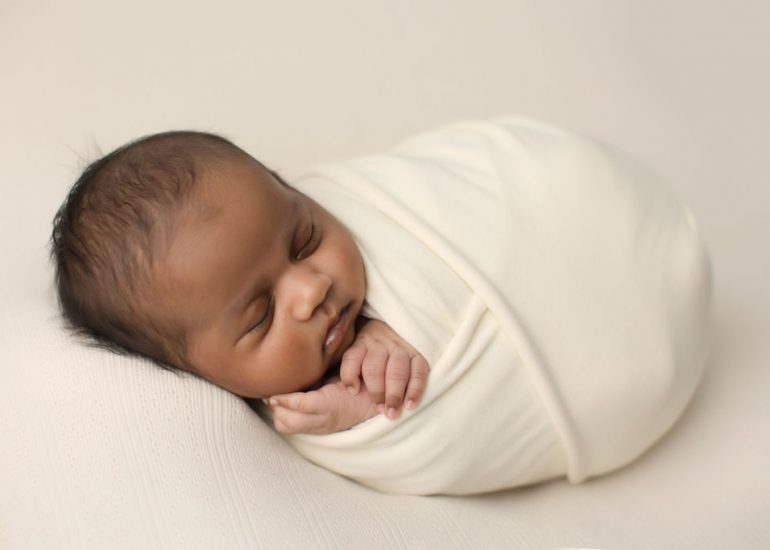 A newborn baby sleeps in a white swaddle with hands out after meeting a doula oshawa