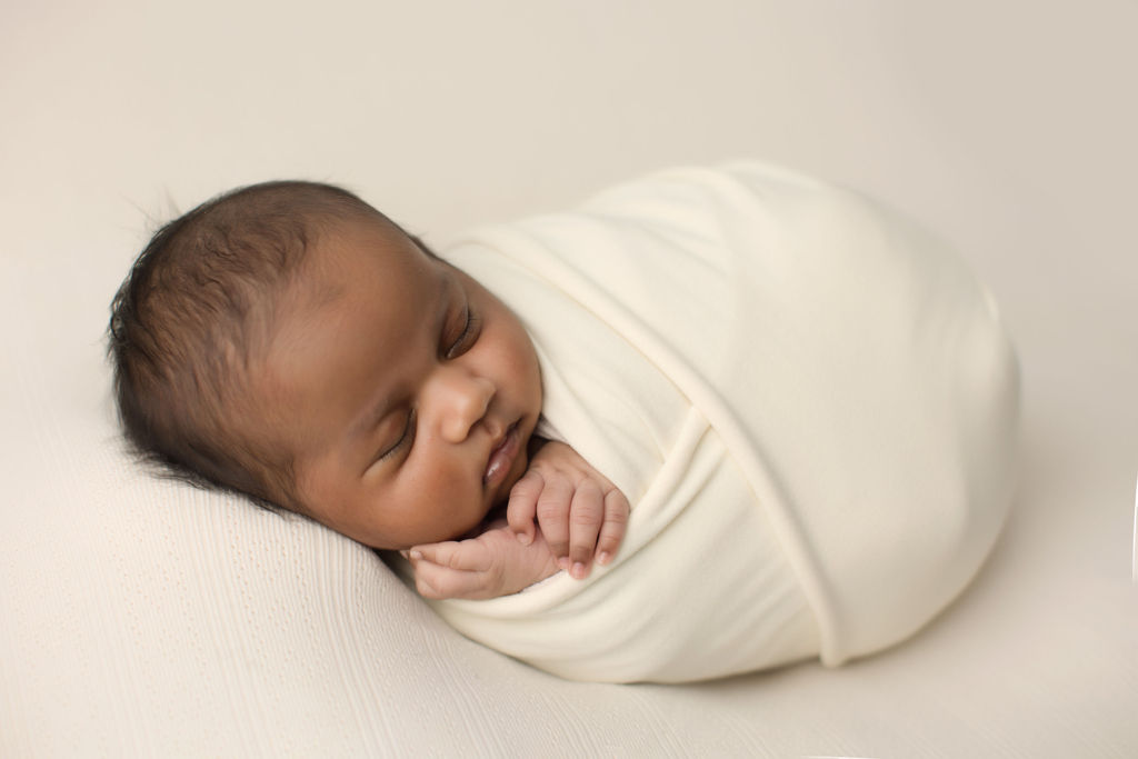 A newborn baby sleeps in a white swaddle with hands out after meeting a doula oshawa