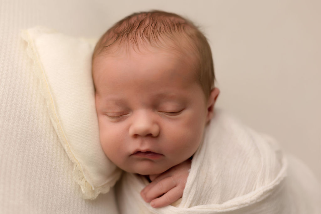 A newborn baby sleeps on a tiny pillow in a white swaddle after working with lactation consultant oshawa