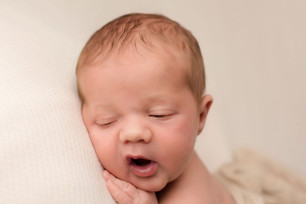 A newborn baby lays on a white bed with mouth open after meeting lactation consultant oshawa