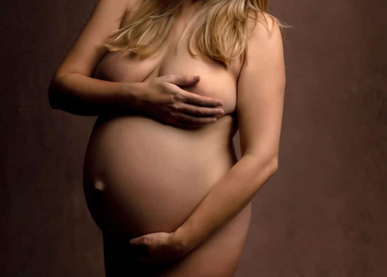 A mother to be holds her bump while standing in a studio