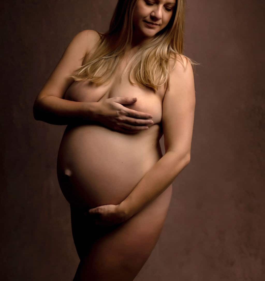 A mother to be holds her bump while standing in a studio