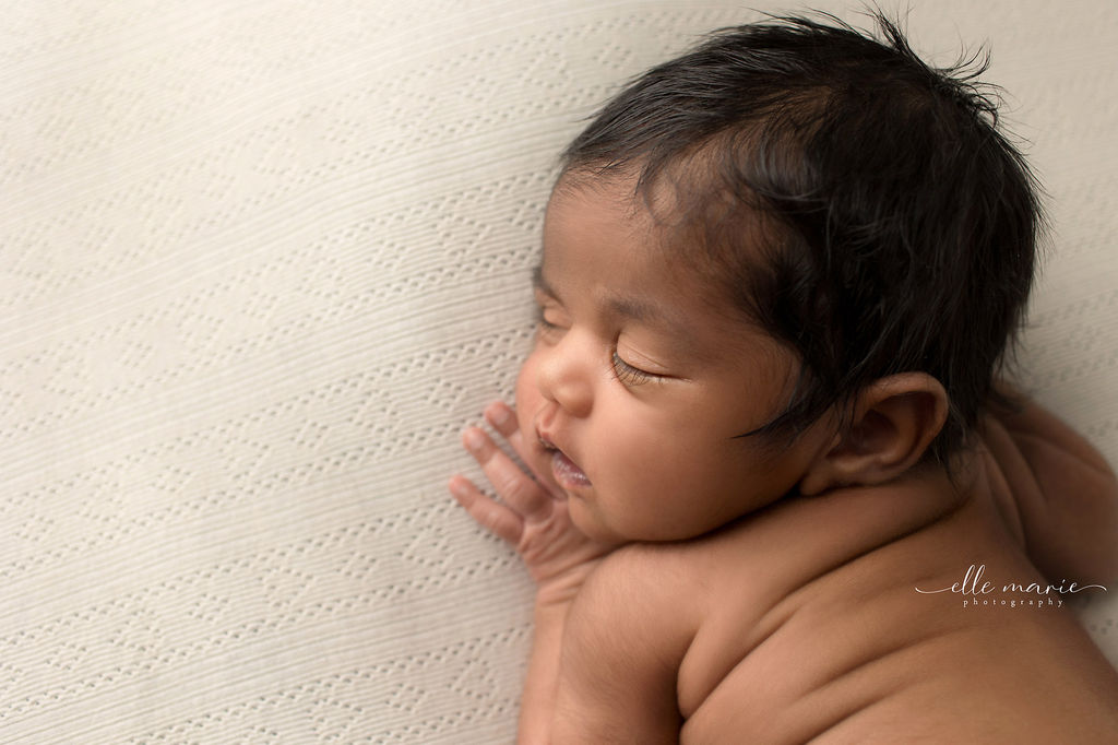 A newborn baby sleeps in froggy pose on a white blanket in a studio thanks to prenatal yoga whitby